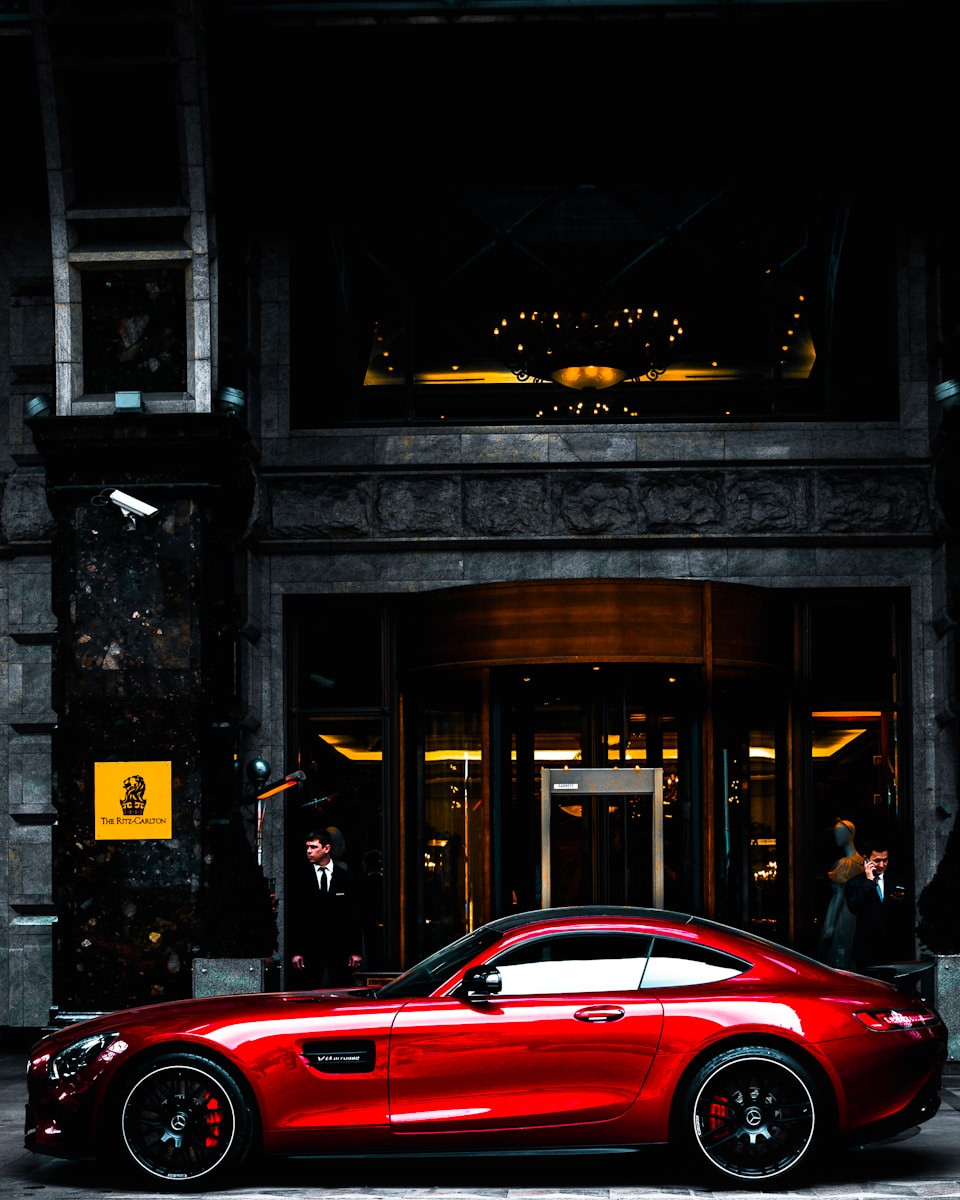 red coupe with auto insurance parked in front of black and gray building during daytime